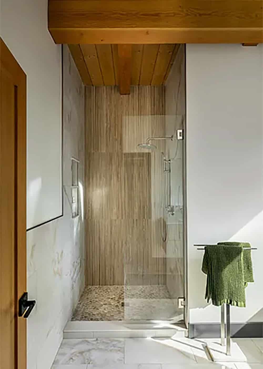 Walk-in shower with a wood-look tile wall, a pebble floor and a rain showerhead, under a wood plank ceiling