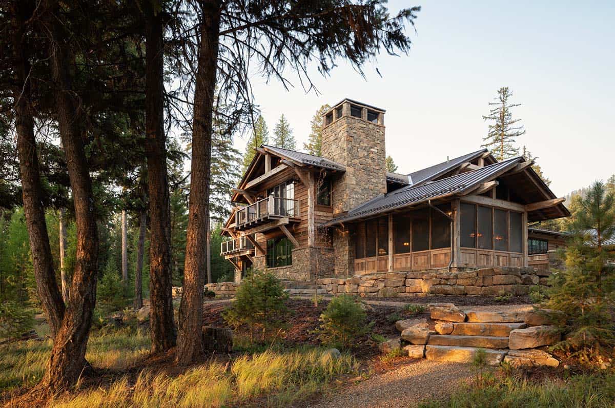 Rustic Montana lake house with a stone chimney and screened porch among pines