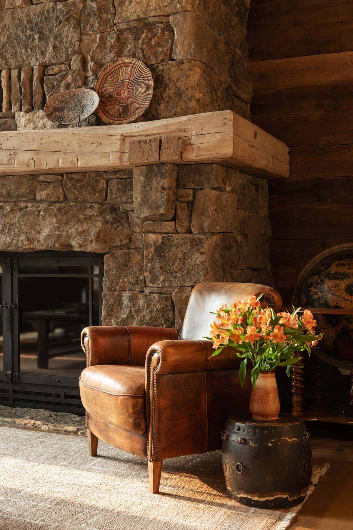 Leather club chair beside the stone fireplace with orange alstroemeria