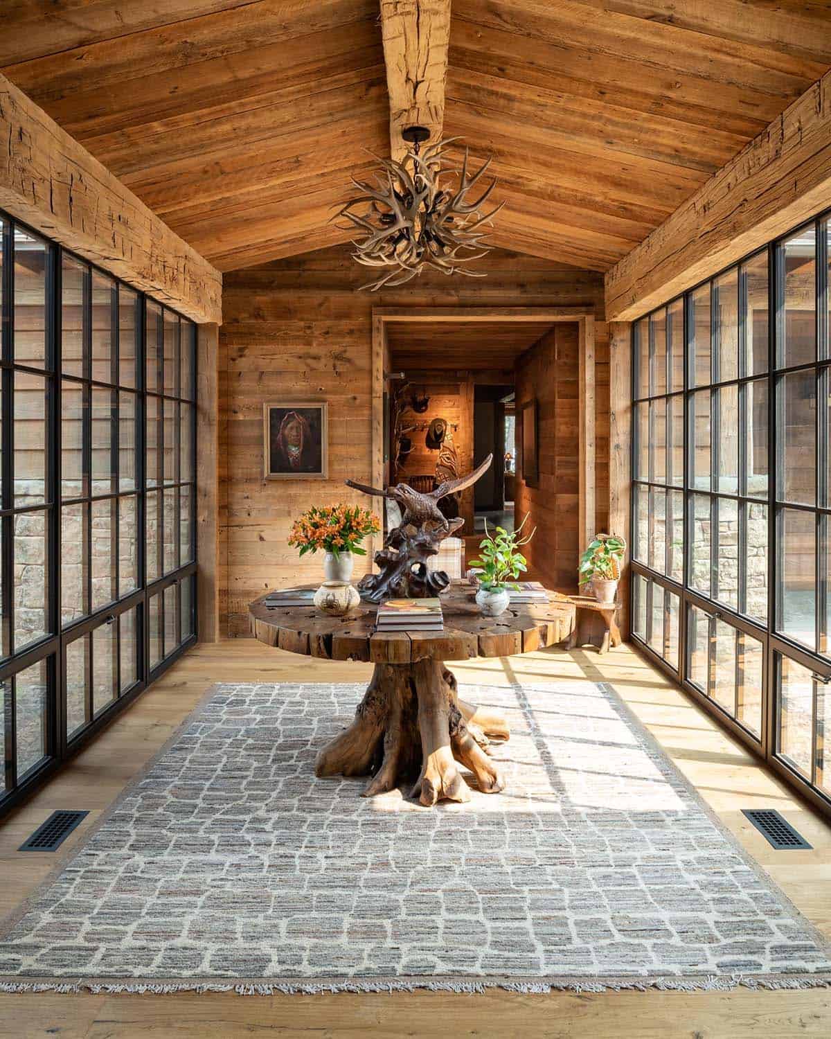 Glass-walled hallway with a root-base table and antler chandelier