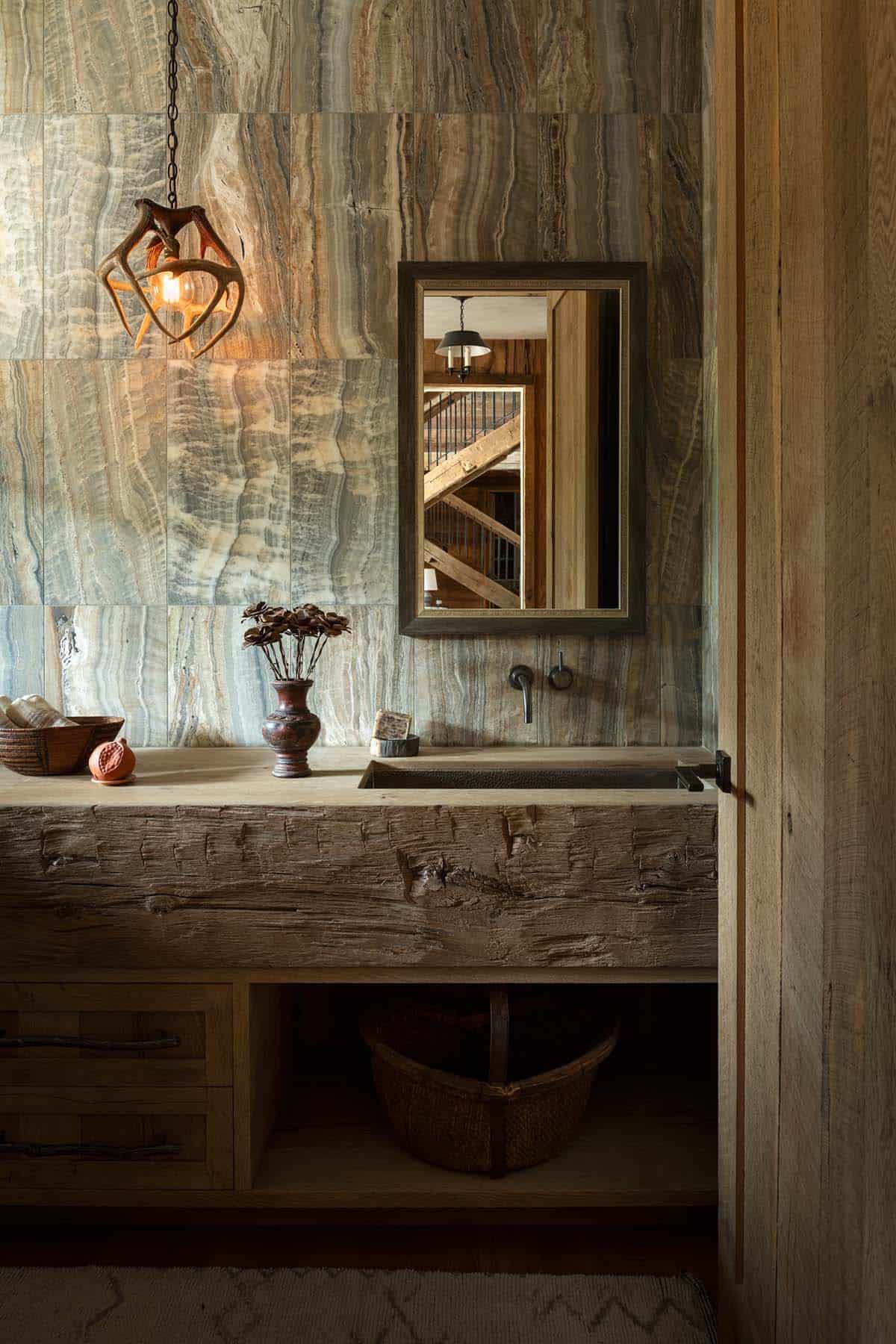 Powder room with veined stone walls, antler pendant, and hewn beam vanity