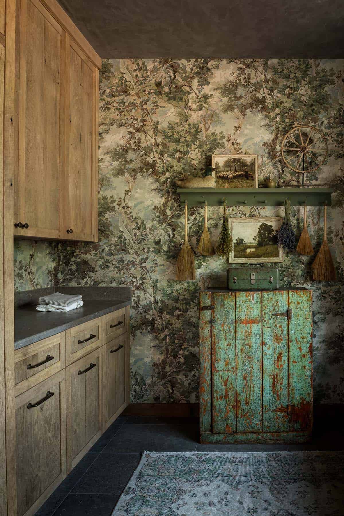 Laundry room with forest wallpaper, green antique cupboard, and hanging brooms