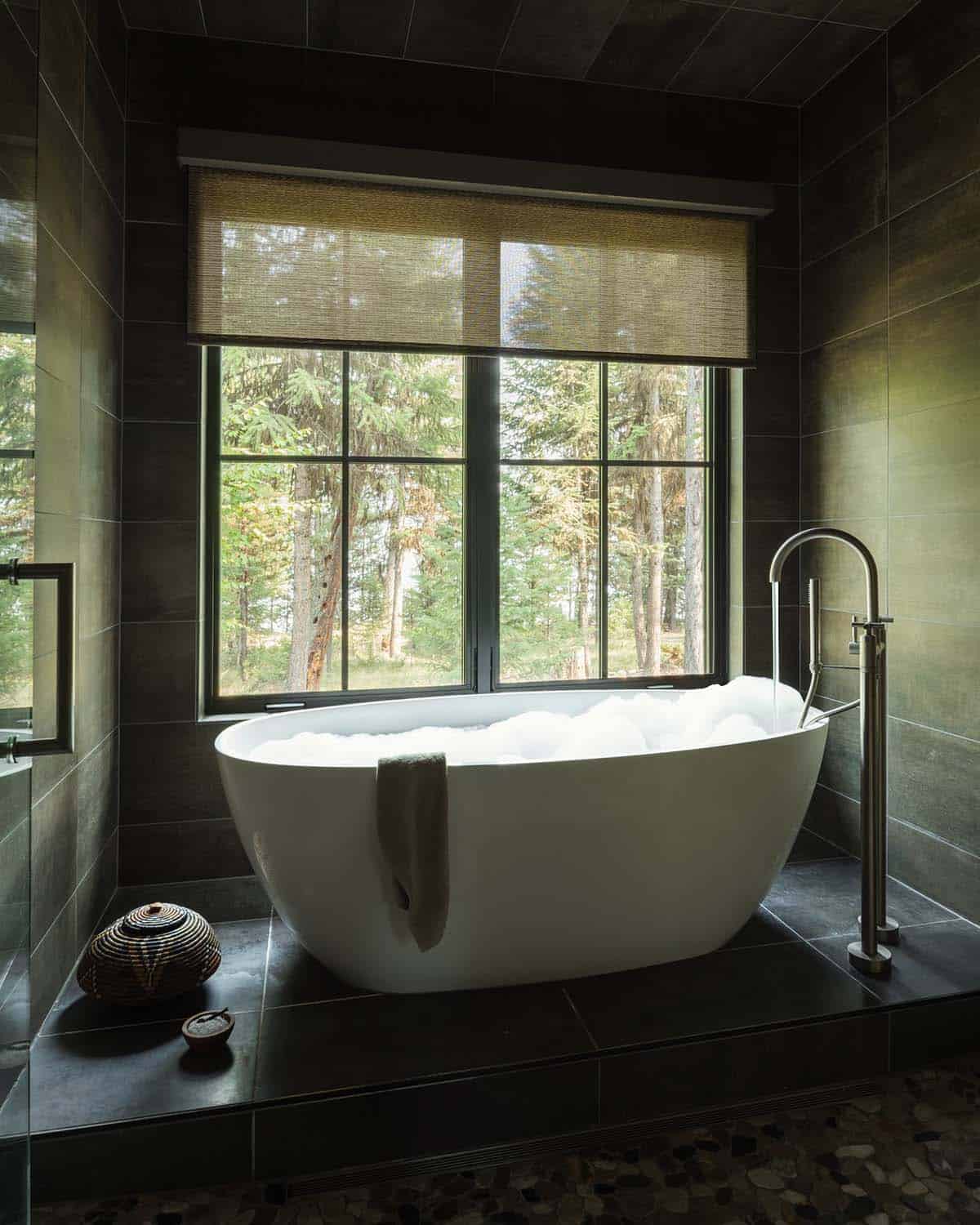 Freestanding tub on a stone platform below a forest-view window