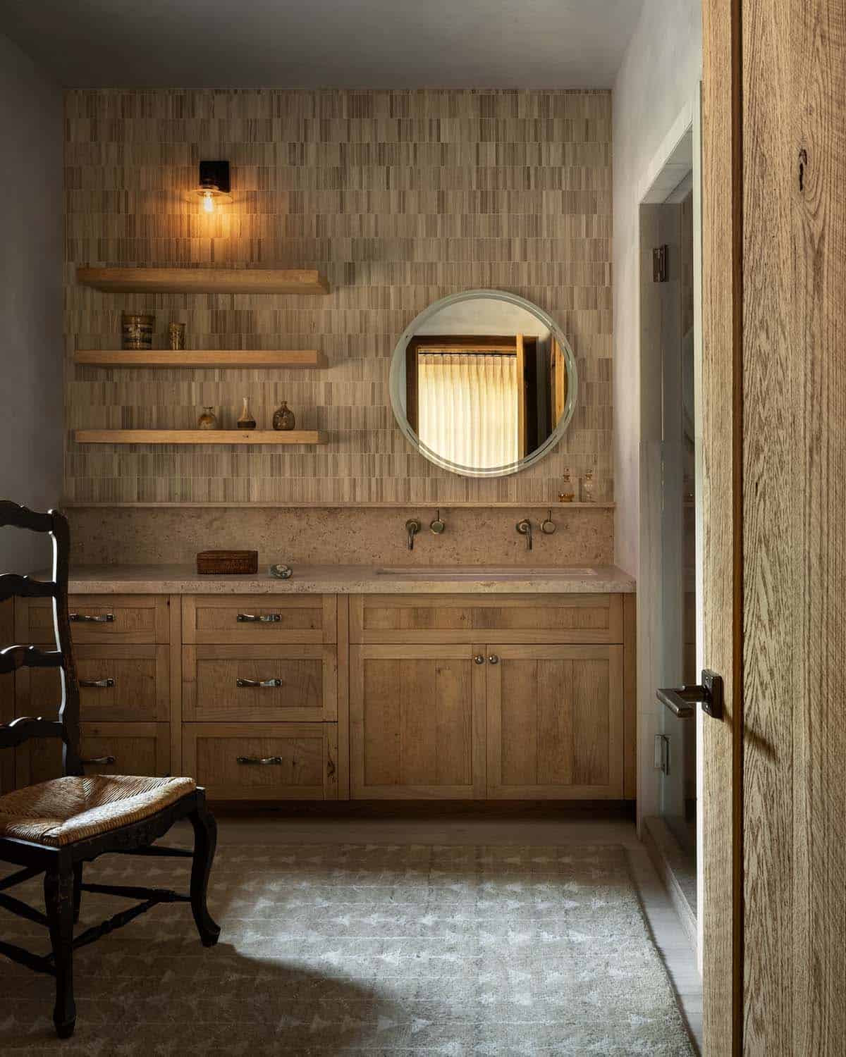 Bathroom with oak vanity, stone counter, and round mirror