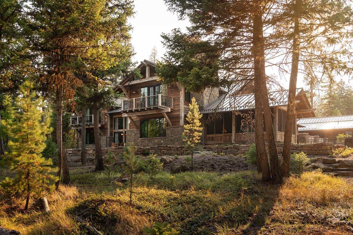 Lake house exterior with balconies and stone base seen through the forest