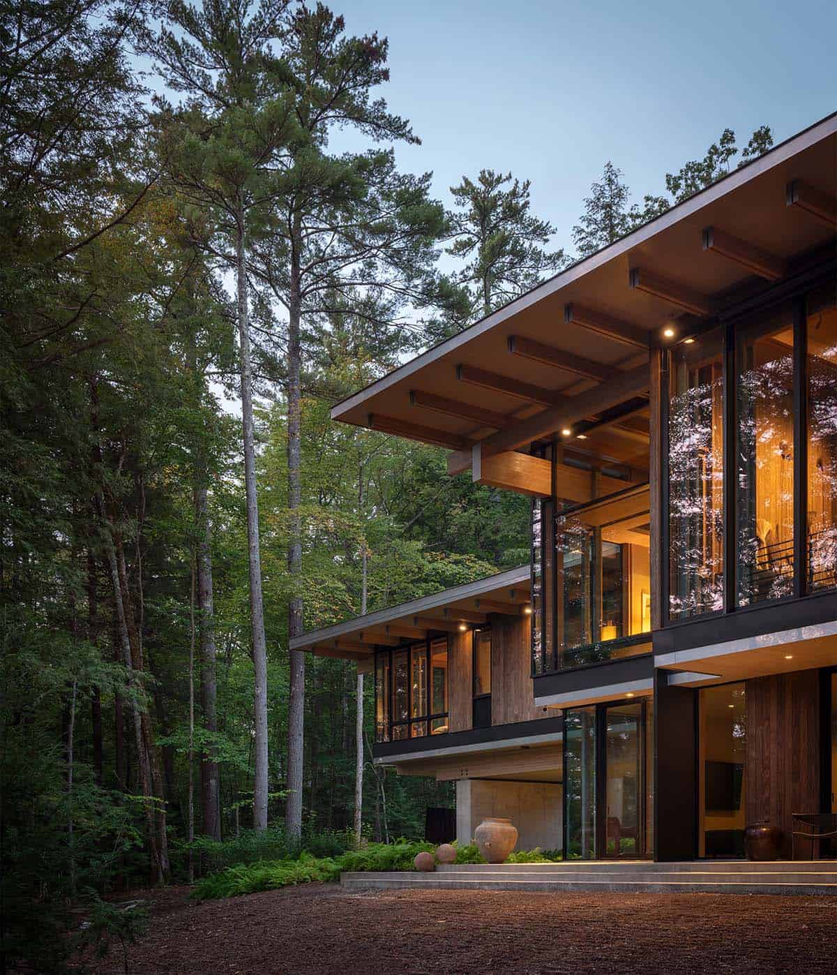 Corner of the lake house at dusk with deep roof overhangs and tall pines
