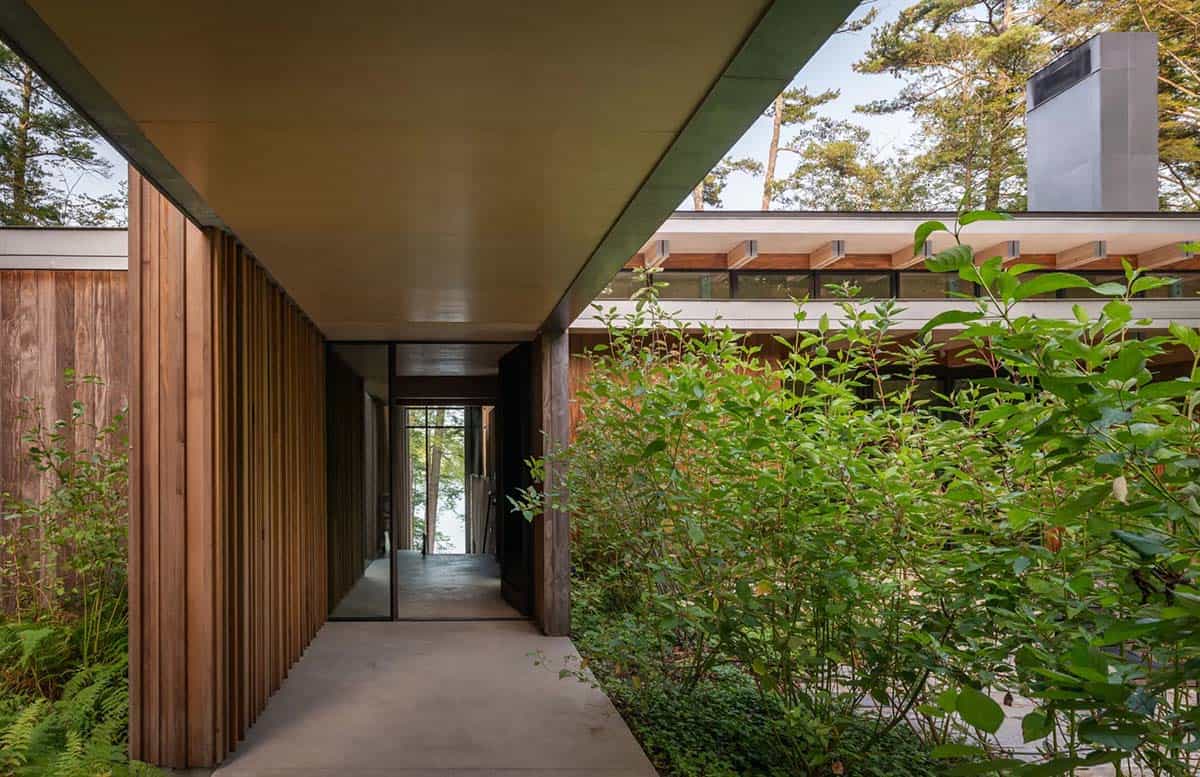 Covered entry walkway with cedar slats leading to a glass door and lake view