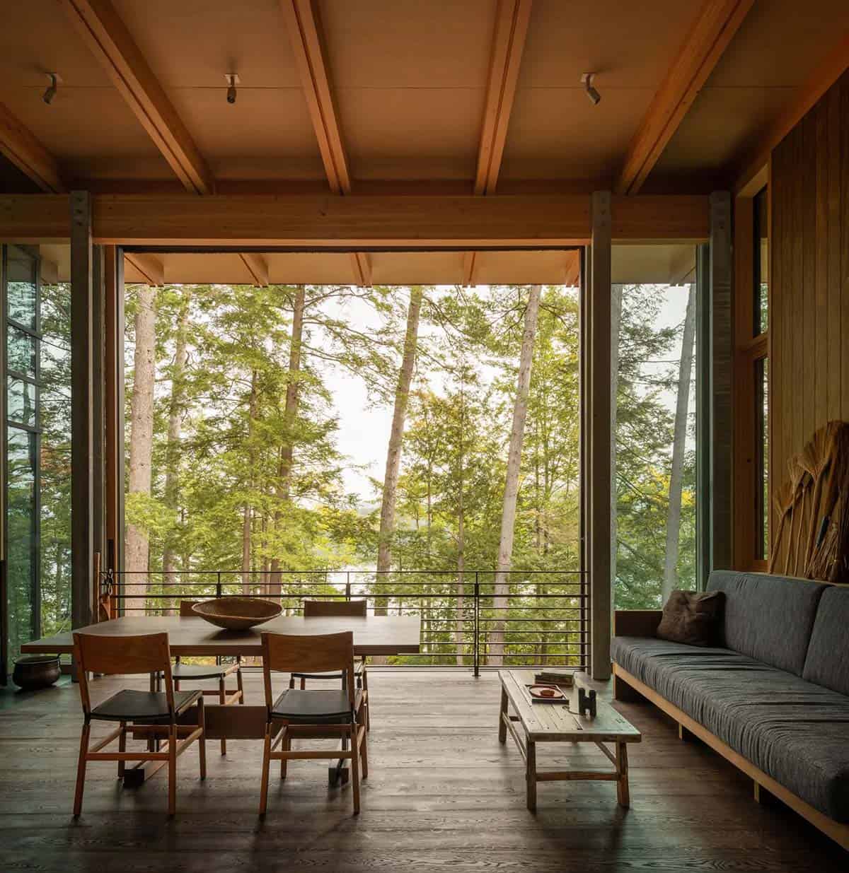 Screened porch with a wood dining table, cushioned bench, and forest views to the lake