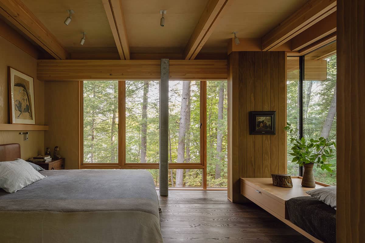 Primary bedroom with a steel column, window seat, and forest views