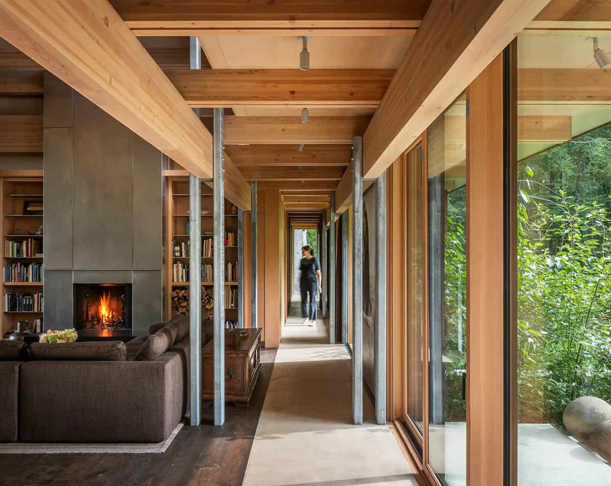 Steel fireplace beside a long hallway leading to a forest window
