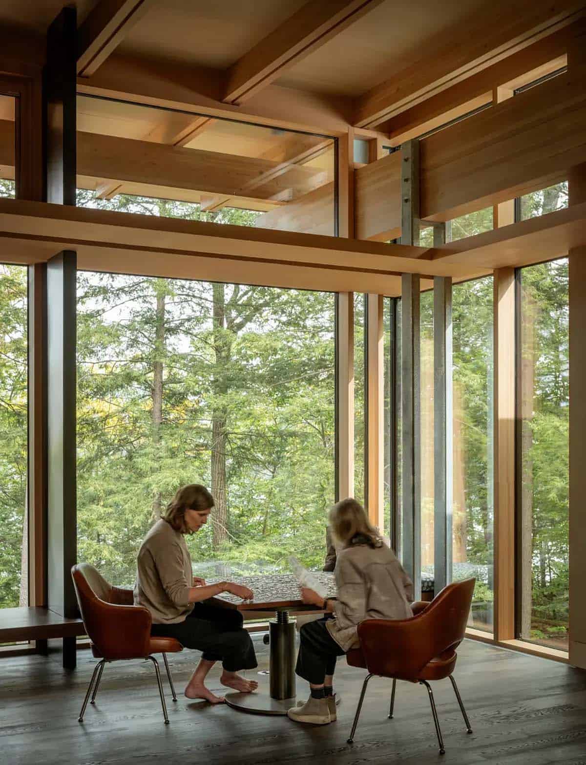 Two women working on a puzzle at a game table by tall windows
