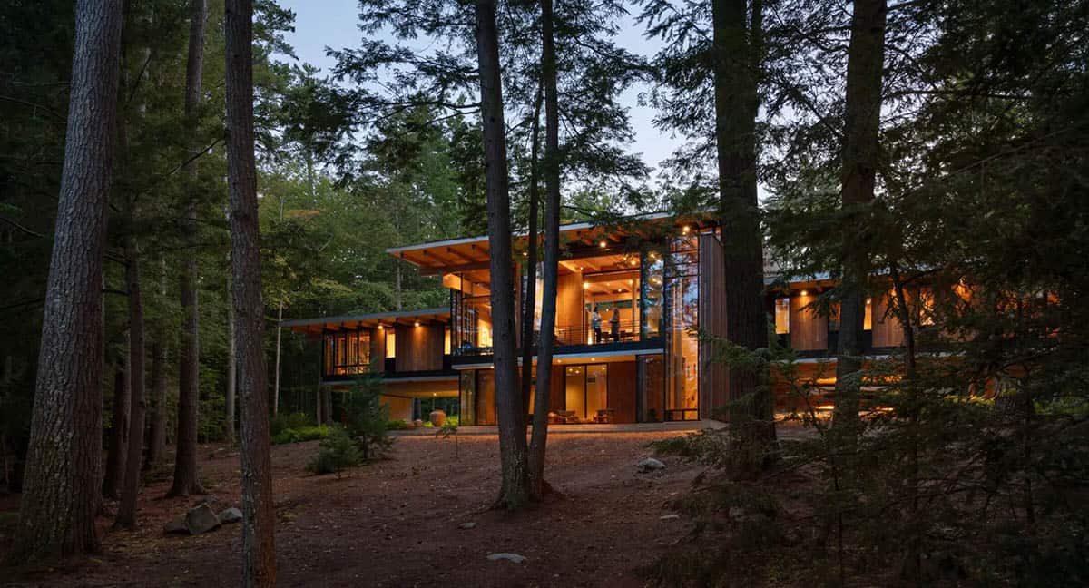 Lake house glowing at dusk among tall pine trees