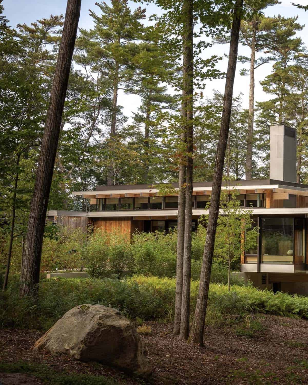 Lake house with clerestory windows and a steel chimney behind a large boulder