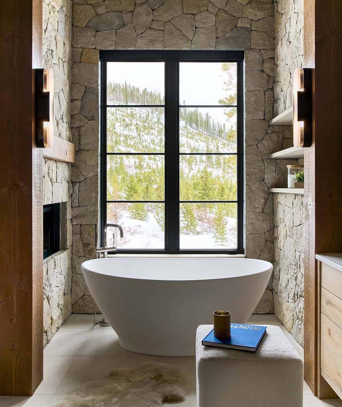 Freestanding tub between stone walls below a forest view window