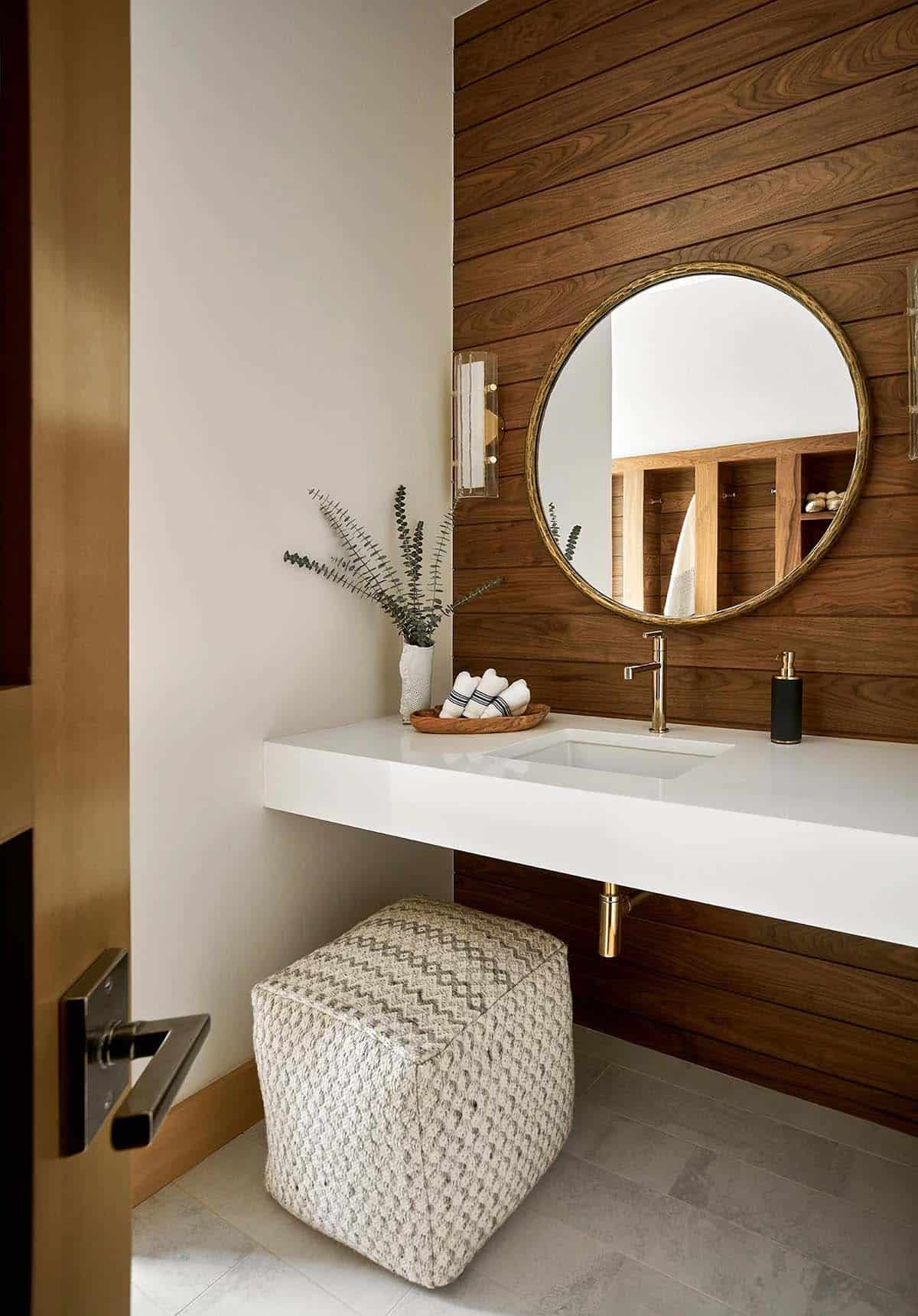 Powder room with walnut plank wall, floating vanity, and round brass mirror