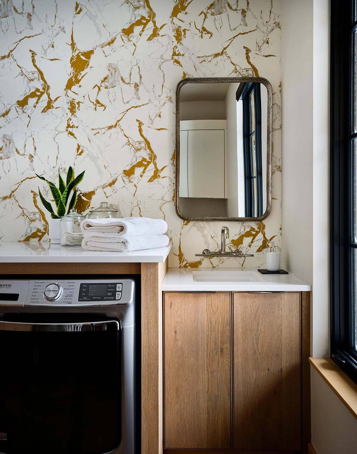 Laundry room with gold-veined wallpaper and an oak sink cabinet