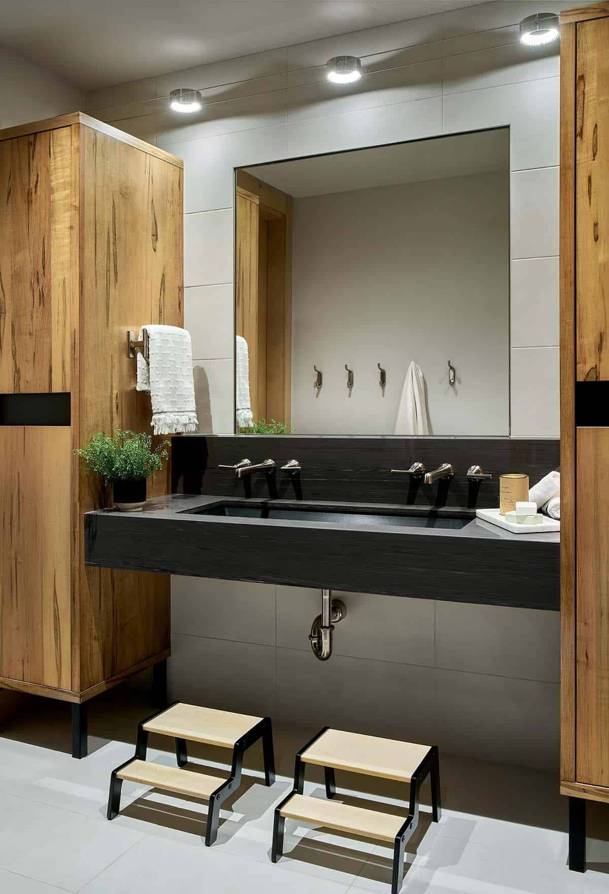 Kids' bathroom with black trough sink, maple cabinets, and step stools