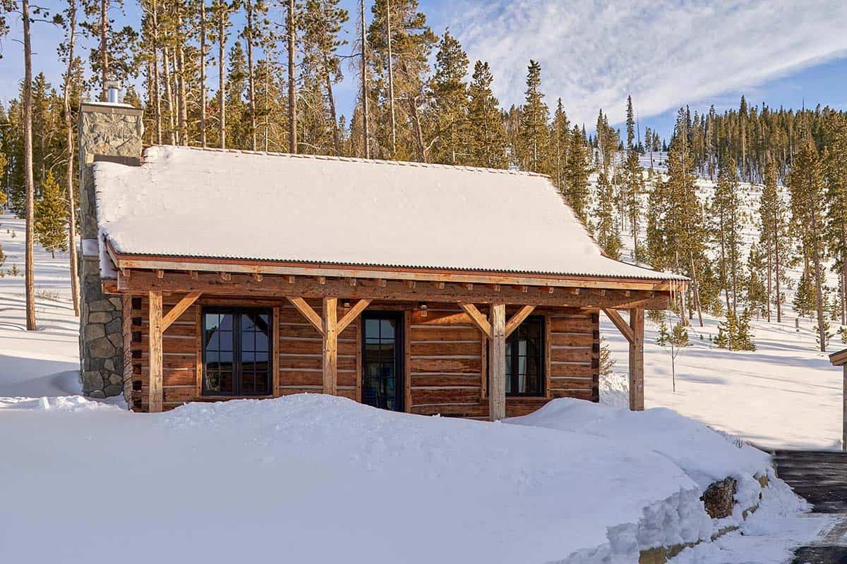 Reclaimed log cabin with covered porch and stone chimney in the snow