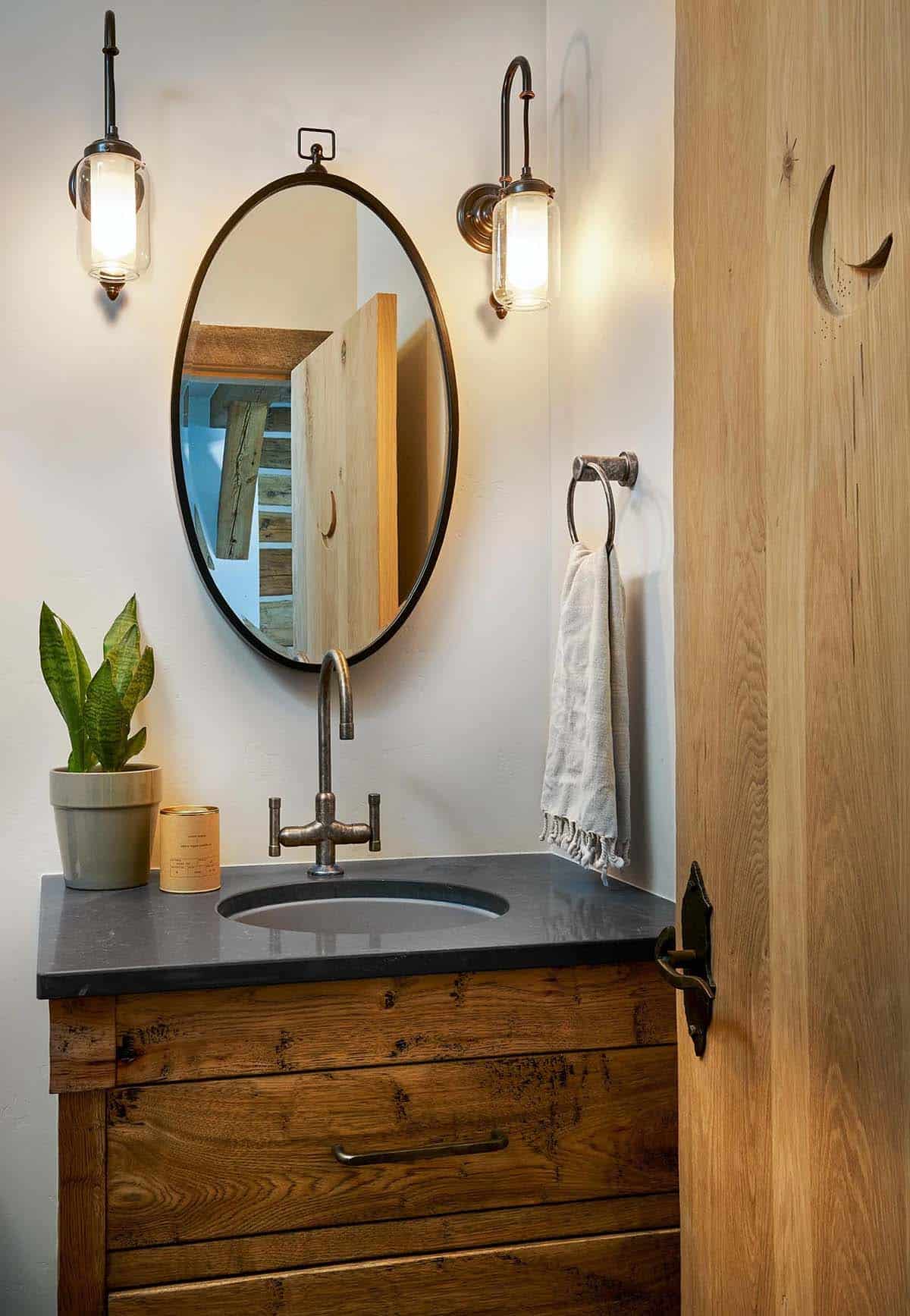 Powder room with oval mirror, lantern sconces, and a moon cutout door
