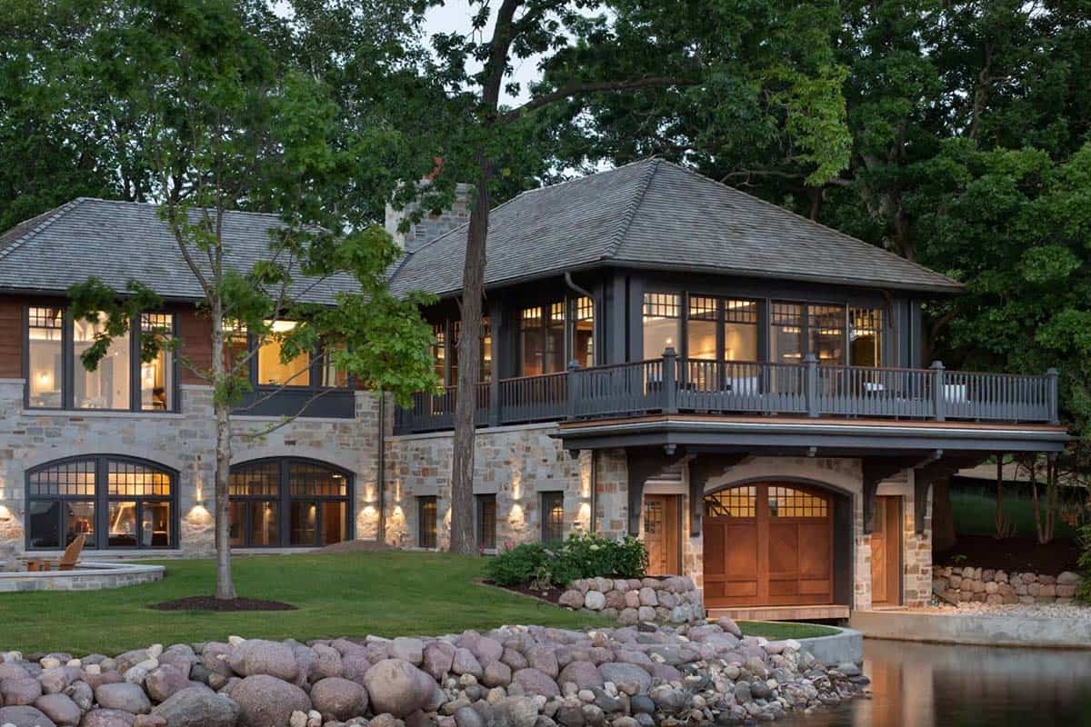 Stone boathouse with arched wood boat door and lakeside deck at dusk