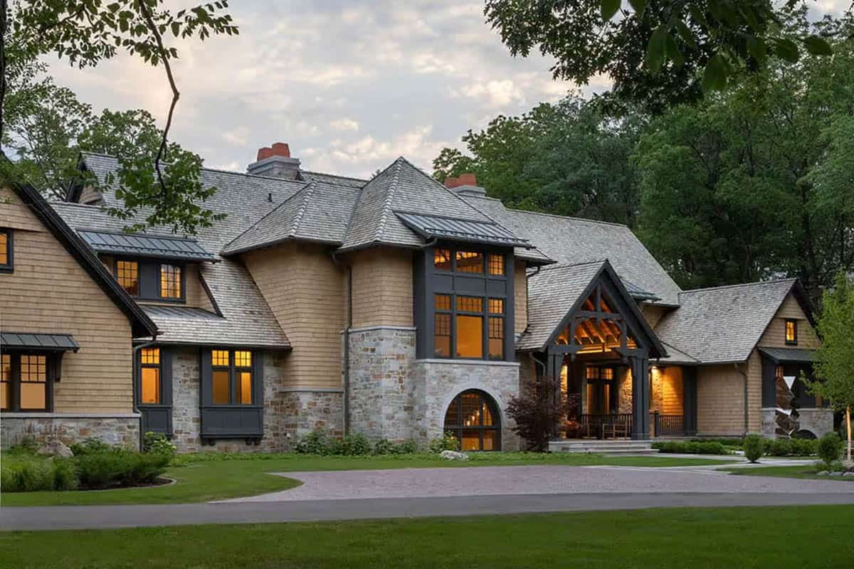 Cedar shingle house with stone base, arched window and glowing entry porch at dusk