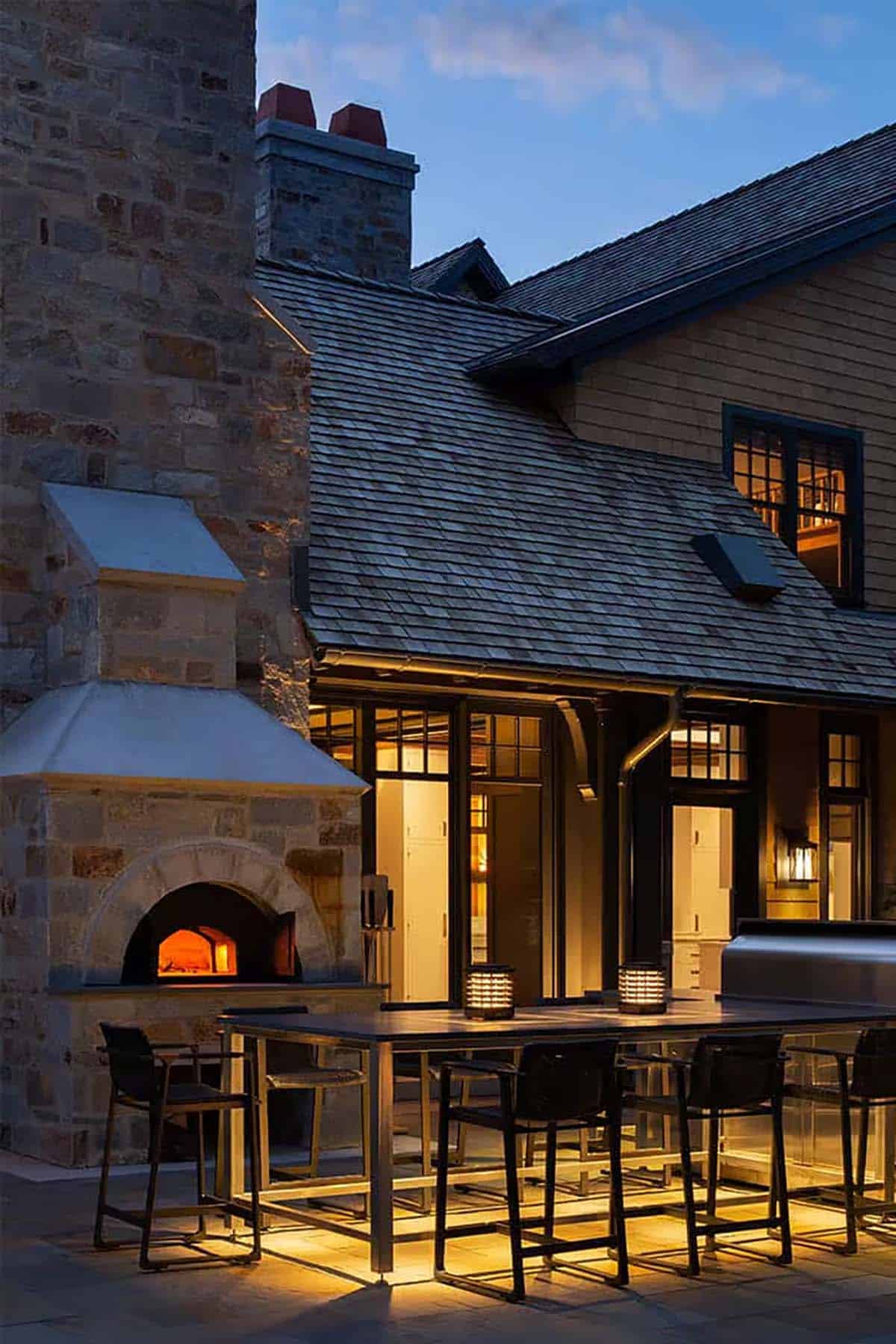 Outdoor bar table beside a stone wood-burning pizza oven at dusk