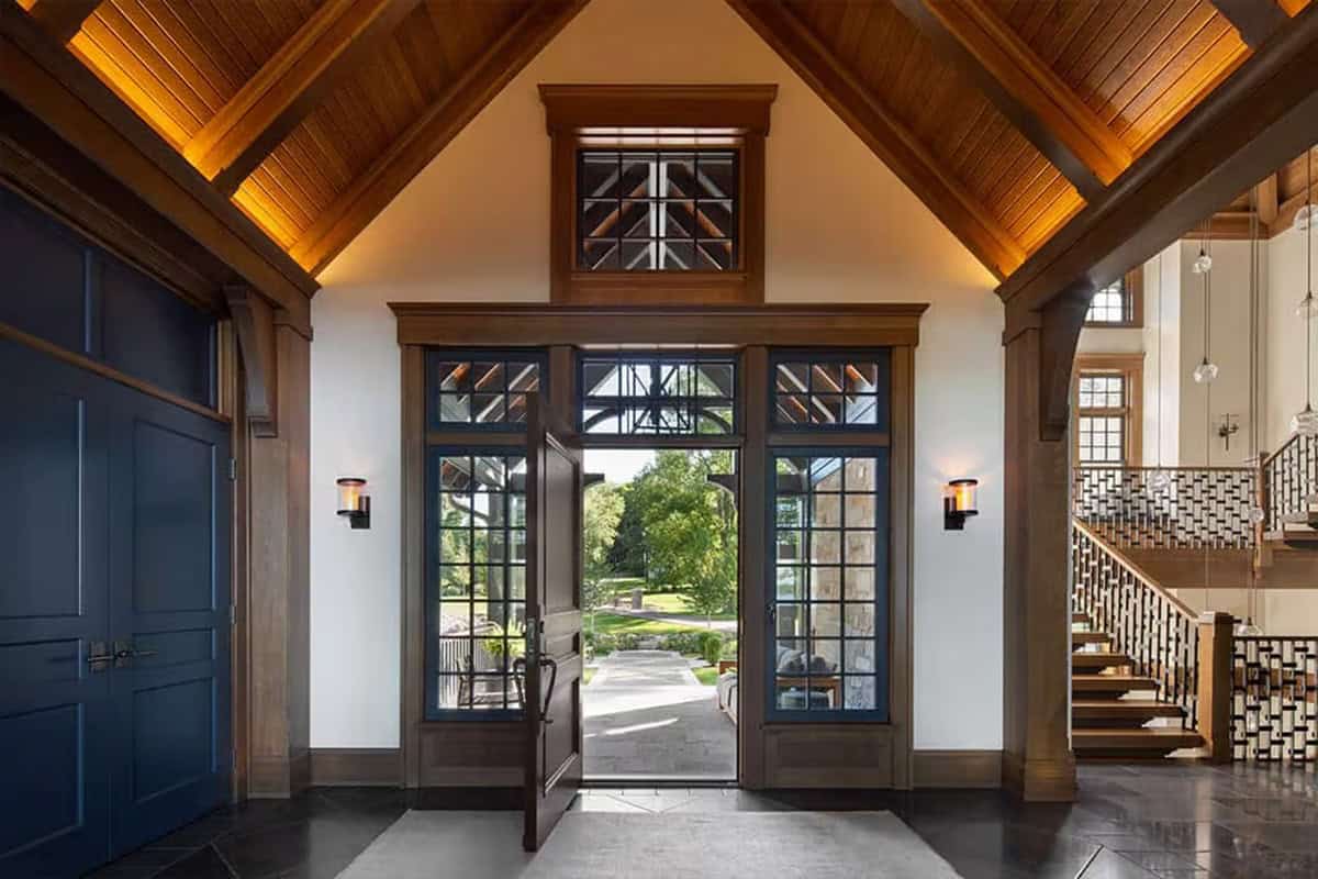 Foyer with vaulted wood ceiling and open front door framed by navy windows