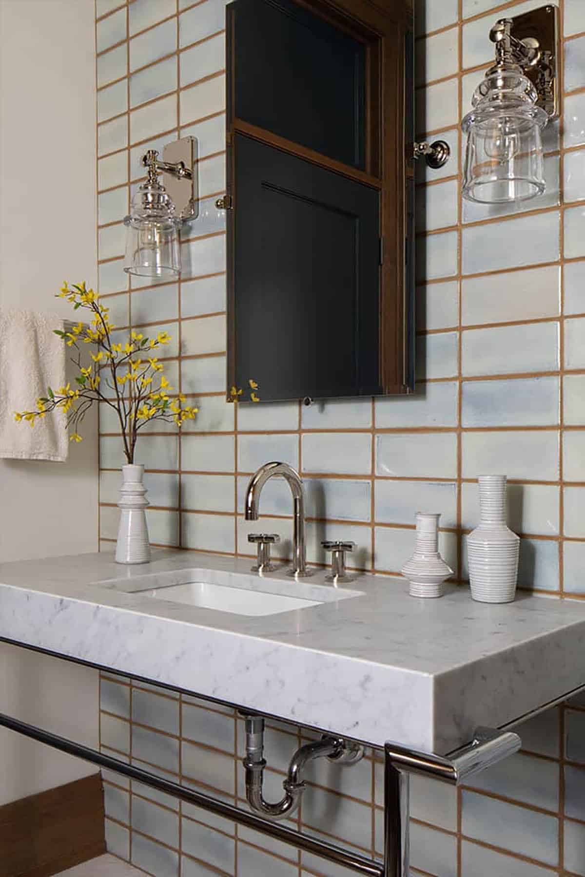 Powder room with pale blue tile, marble console sink and glass sconces