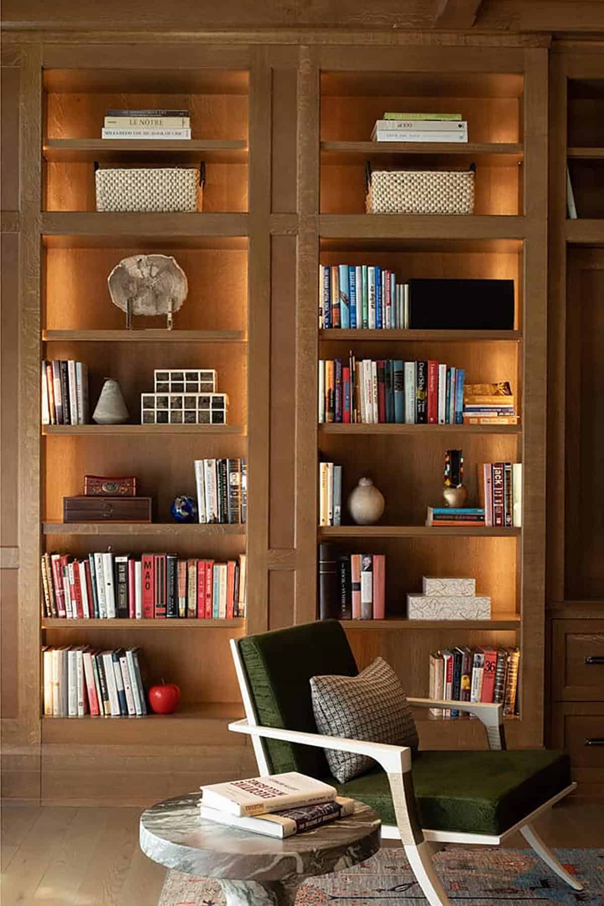 Backlit oak bookshelves with green velvet chair and marble side table