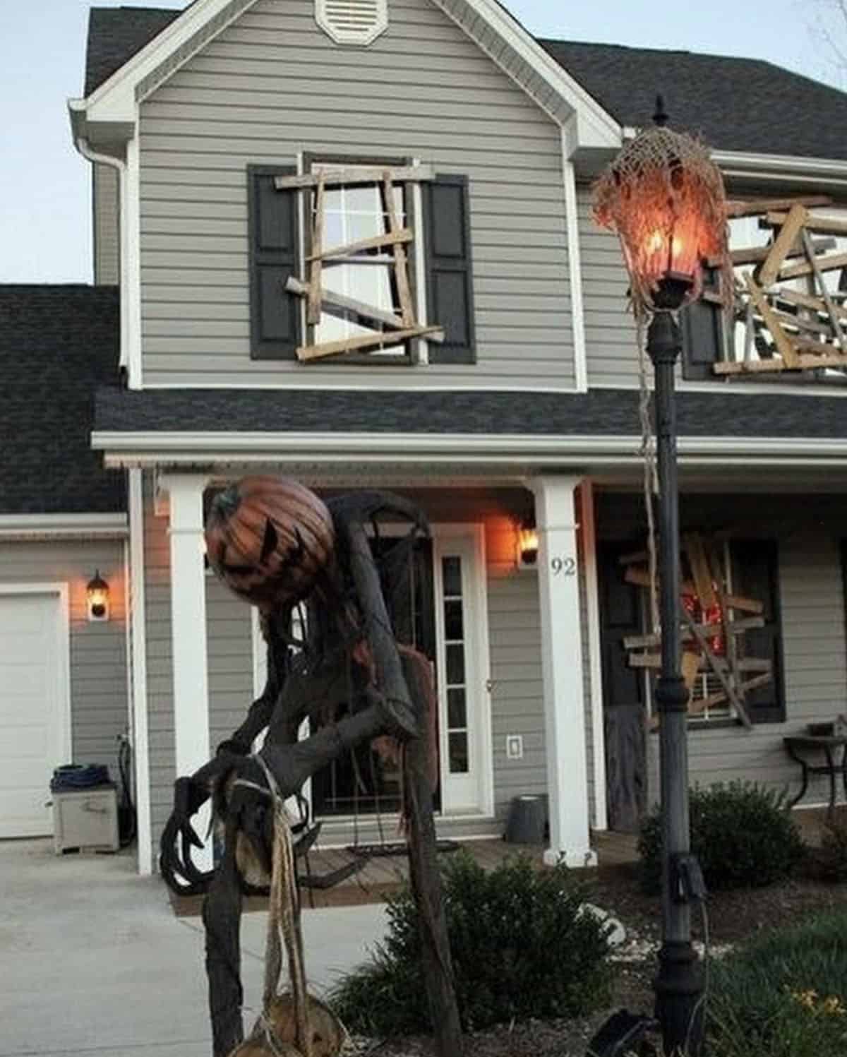 Gray two-story house with weathered boards nailed across the windows and a glowing lantern post at dusk, a DIY haunted house for Halloween