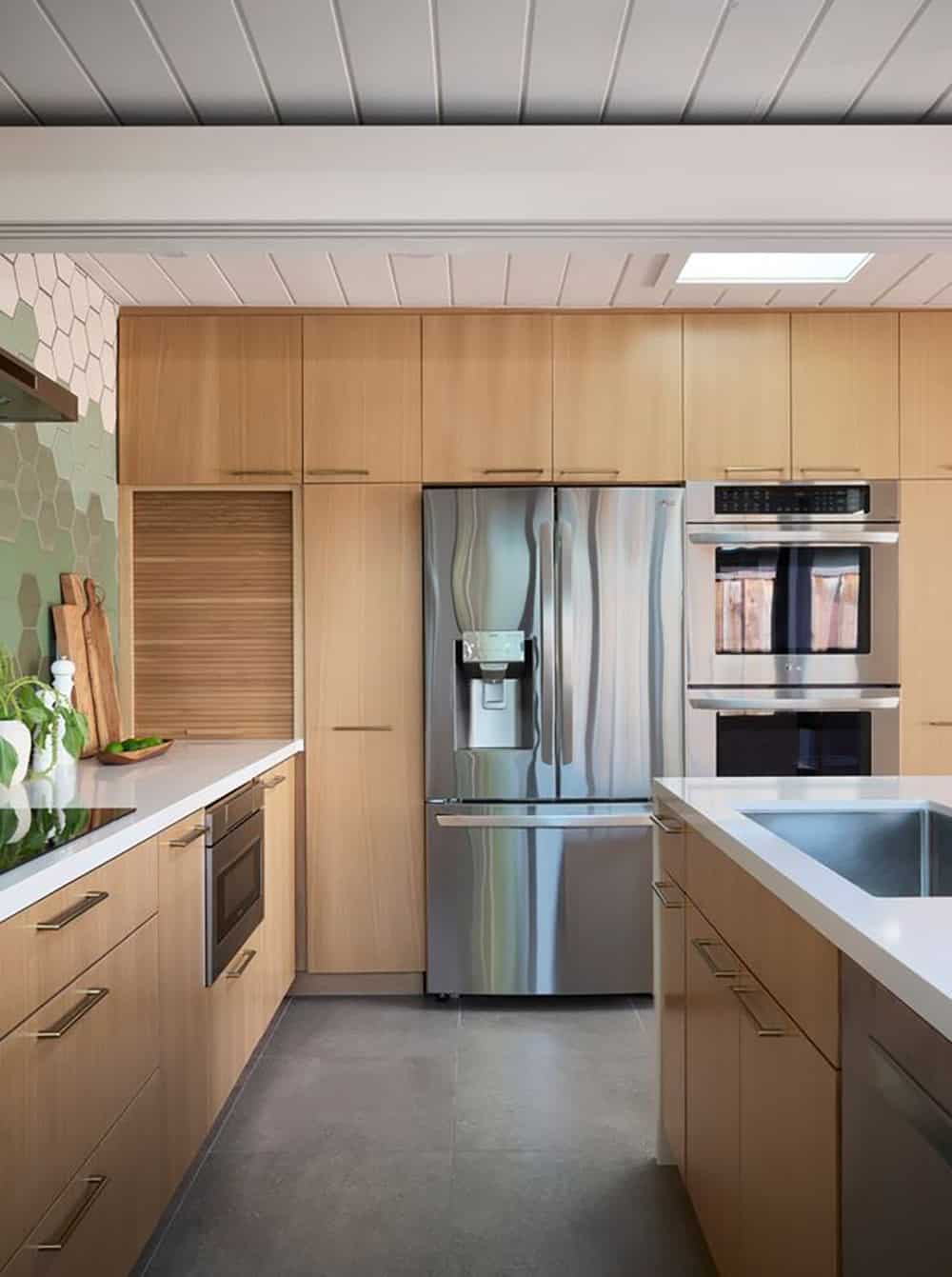 Wall of oak cabinetry with a stainless French-door refrigerator and double wall ovens beneath a skylight in the white plank ceiling