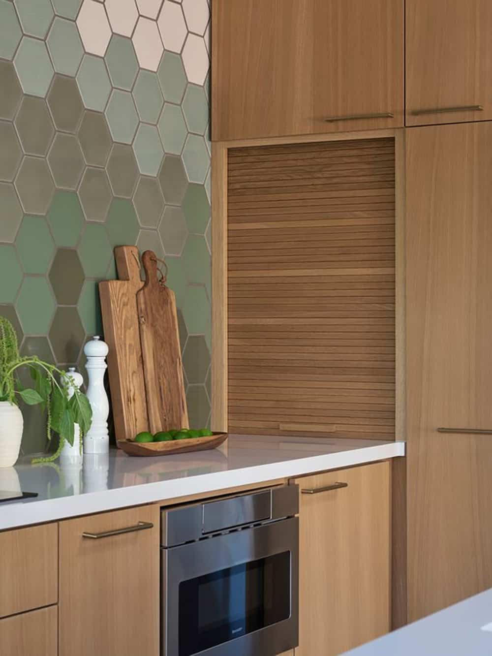 Oak tambour appliance garage beside a white quartz counter, drawer microwave and green hexagon tile backsplash