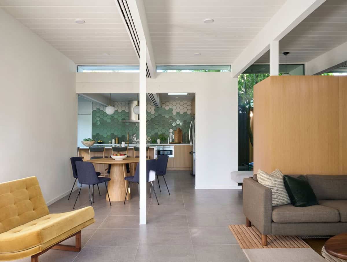 Open great room with a large-format gray tile floor, a mustard velvet chair and gray sofa, looking toward the dining area and kitchen