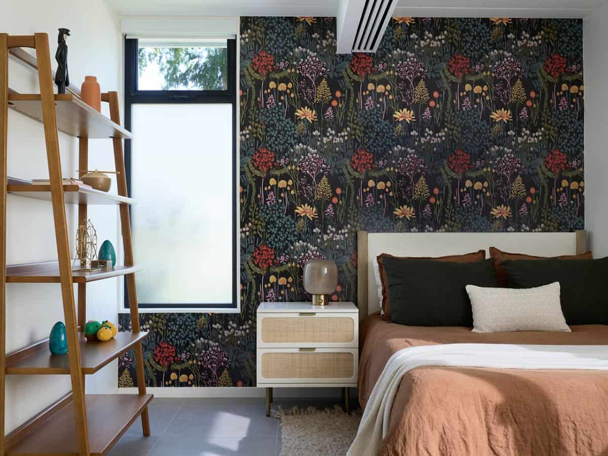 Kid's bedroom with a dark wildflower wallpaper accent wall, rust and green linen bedding, a cane nightstand and a wood ladder bookshelf