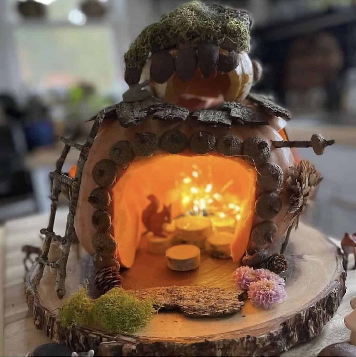 pumpkin fairy house with acorn cap doorway, bark shingles, fairy lights, and squirrel figurine inside
