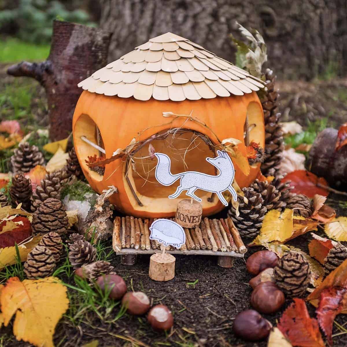jack-o’-lantern with upcycled cardboard shingle roof, round twig windows, twig porch, and paper fox and hedgehog figures