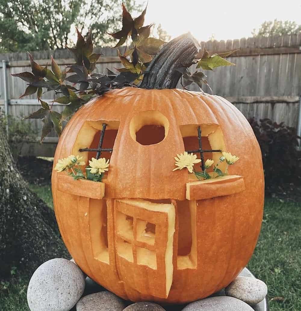 carved jack-o'-lantern with open front door, twig windows, and window boxes with yellow mums