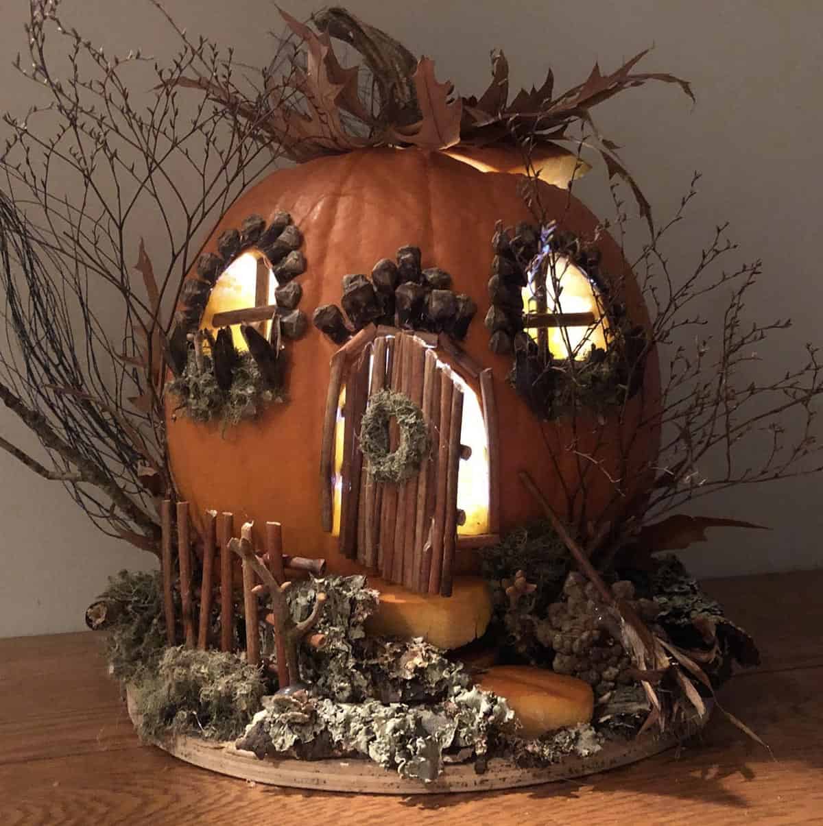 fairy cottage pumpkin with twig door, moss wreath, pinecone window trim, and leaf roof