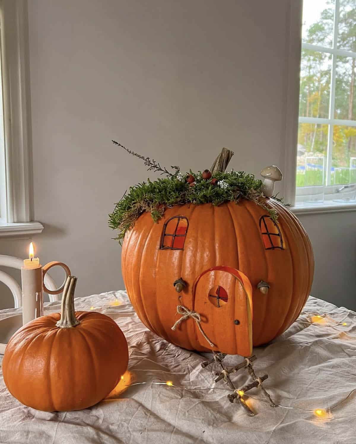 orange fairy house pumpkin with moss roof, twig windows, open door, acorn lanterns, and twig ladder