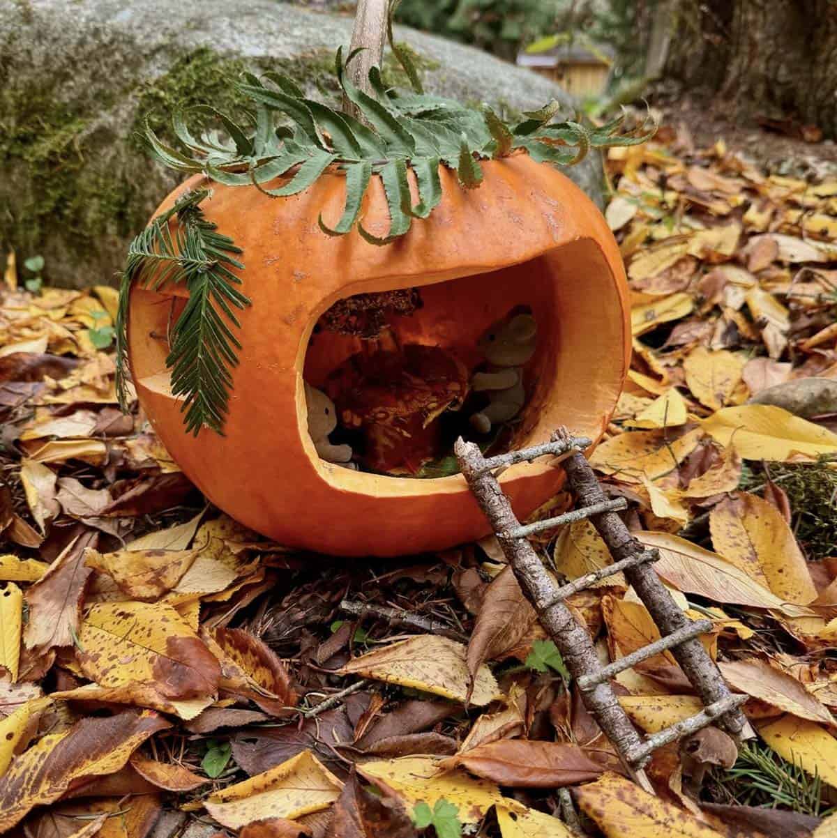 jack-o'-lantern on its side with mouse figurines, fern roof, and twig ladder in fallen leaves