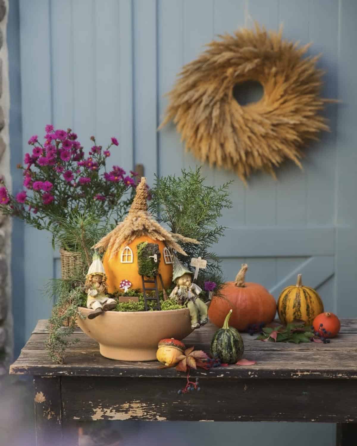 fall centerpiece in a mossy terra-cotta bowl on a rustic table with gourds and a dried grass wreath
