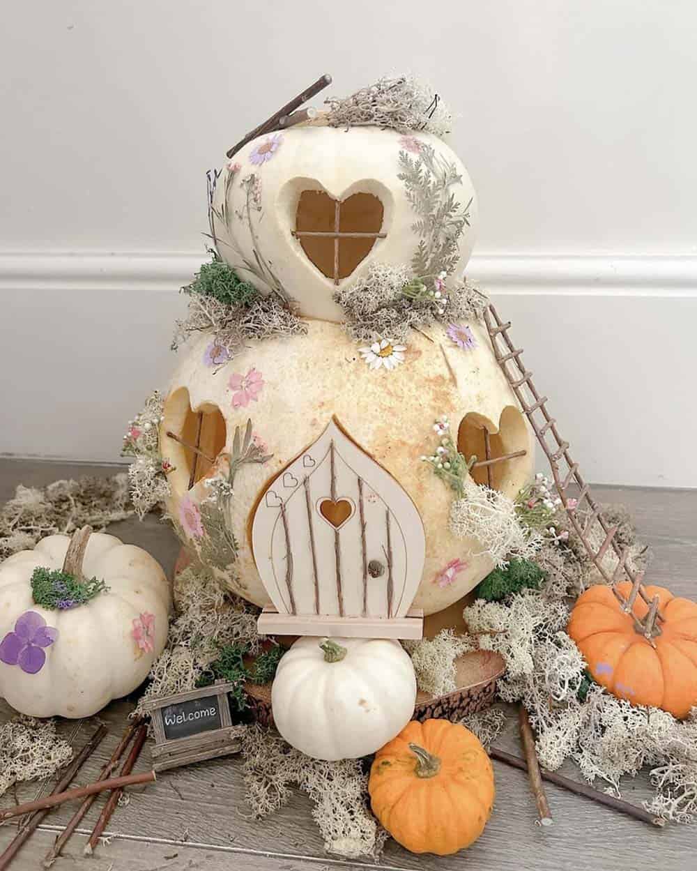 white pumpkin fairy house with heart-shaped windows, pressed flowers, wooden door, and twig ladder