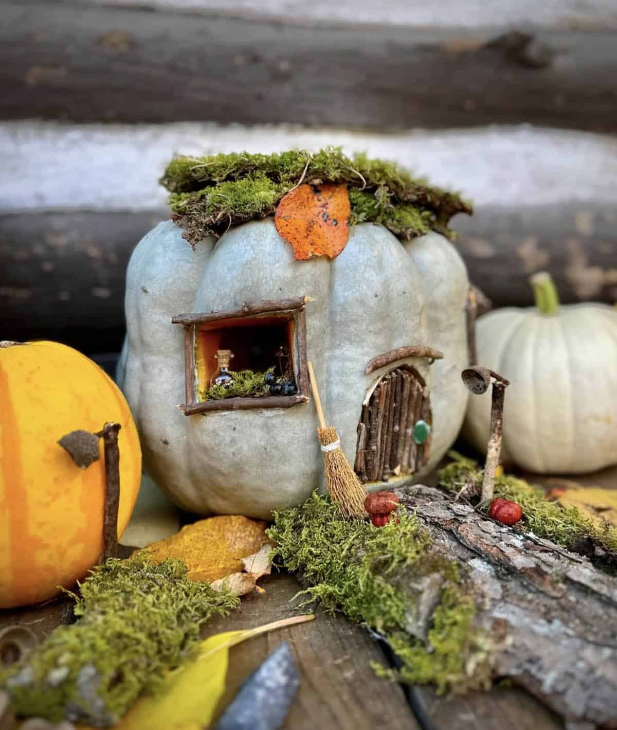 blue-gray heirloom jack-o’-lantern with twig door, potion bottle window, mini broom, moss roof, and acorn cap lampposts