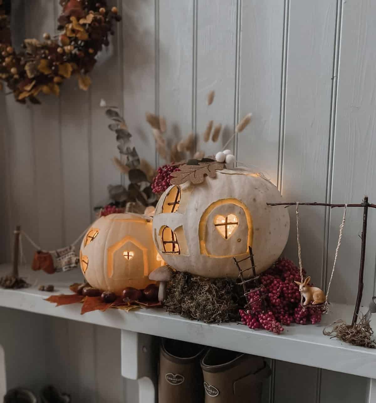 white jack-o'-lanterns on a mudroom shelf with a twig swing, bunny figurine, moss, and autumn leaves