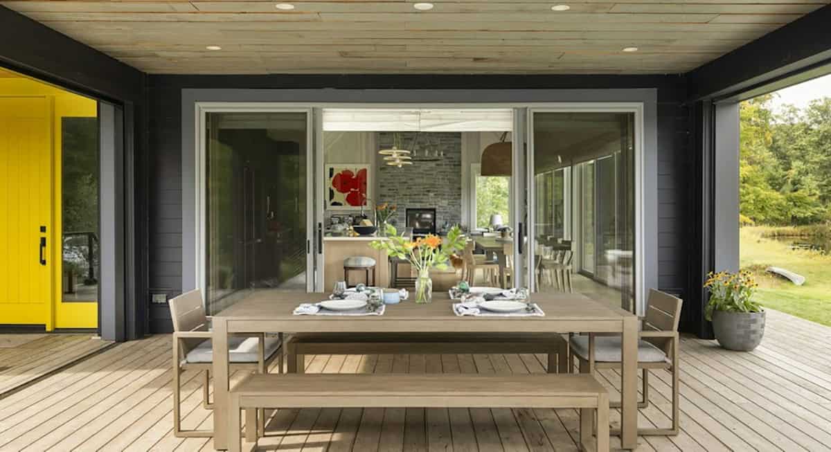 Covered porch with an outdoor dining table and benches, sliding glass doors into the kitchen and a yellow door at left