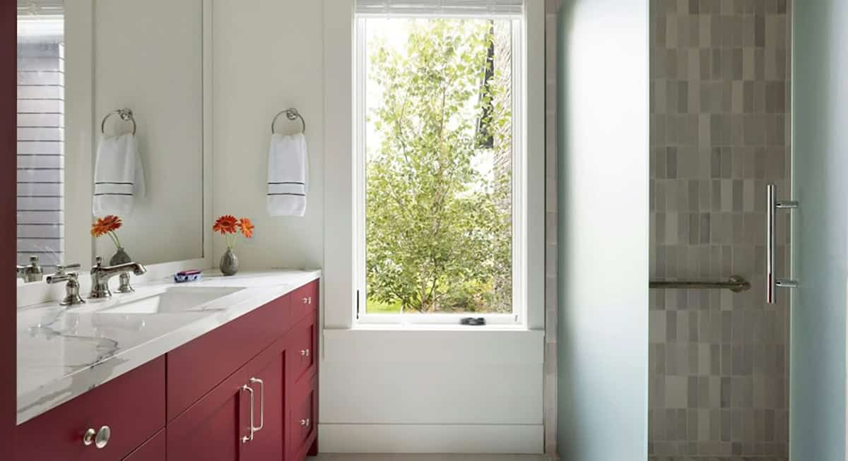 Bathroom with a red vanity, white marble-look countertop, polished nickel faucet, tall window and frosted glass shower door