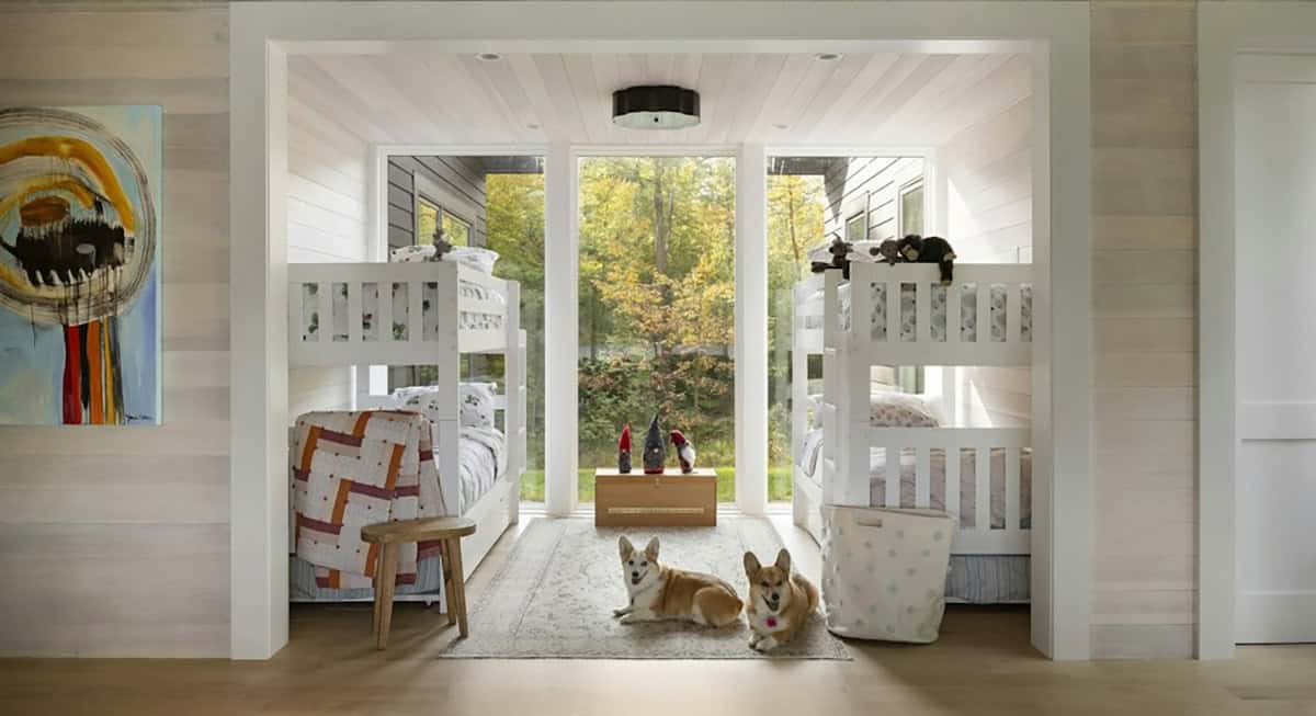 Bunk nook with white bunk beds on either side of a tall window, colorful art on the wall and two corgis lying on a rug