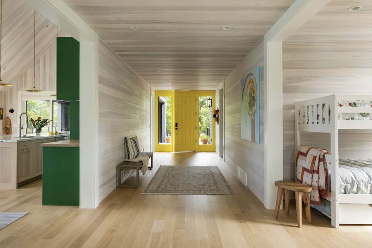 Long whitewashed wood hallway leading to a yellow front door, with the green kitchen at left and a bunk bed nook at right