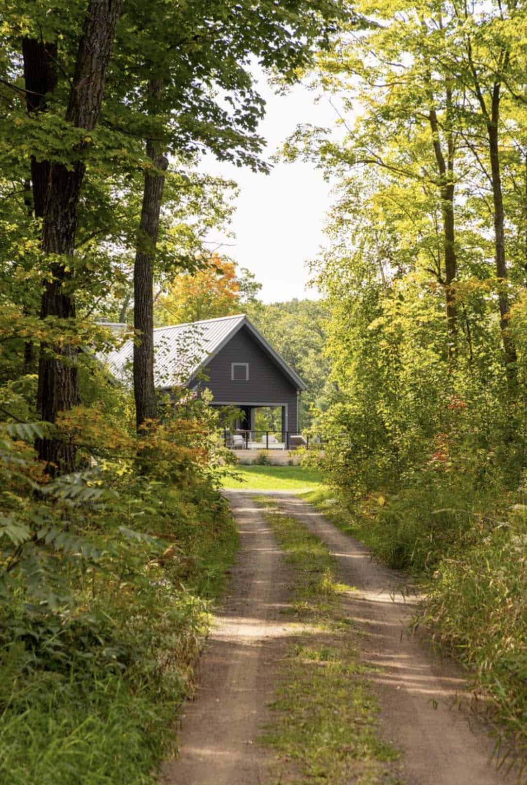 Two-track dirt road through a green and gold forest leading to the dark gray gabled cabin