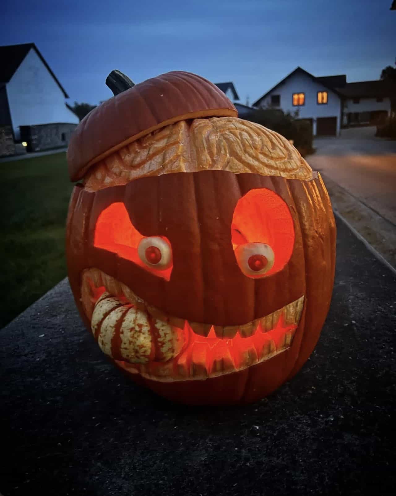 brainy carved pumpkin glowing orange at dusk, with peeled potato eyeballs and a gourd clamped in its toothy grin
